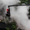 Midtown Manhattan steam rising beside a red traffic light and office building.