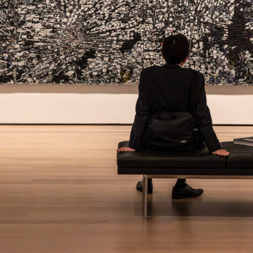 Woman seated on a museum bench viewing a large contemporary abstract artwork