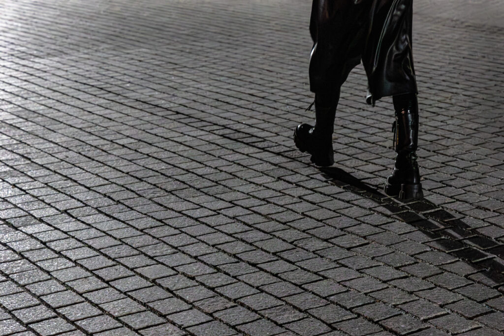 Woman in black combat boots walking alone at night, photographed by Pamela Thomas-Graham — a study in confidence, shadow, and luxury after dark.