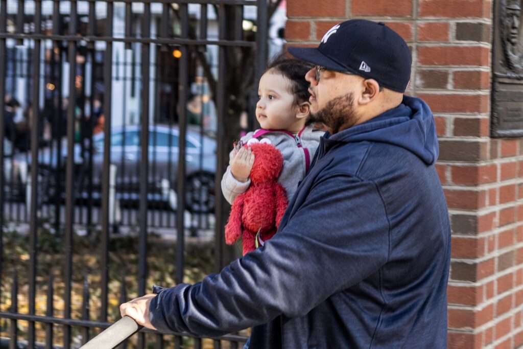 father holding young daughter beside city fence — father-daughter relationship in literature