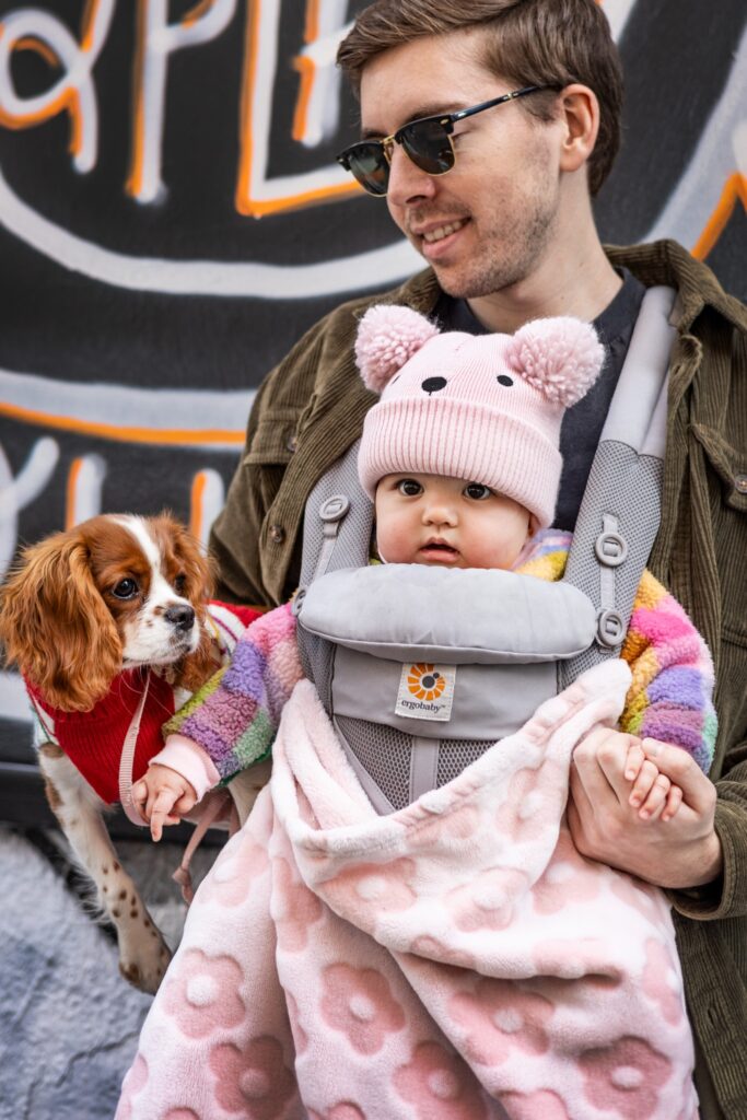 father holding baby girl in a carrier beside a small dog — father-daughter relationship in literature