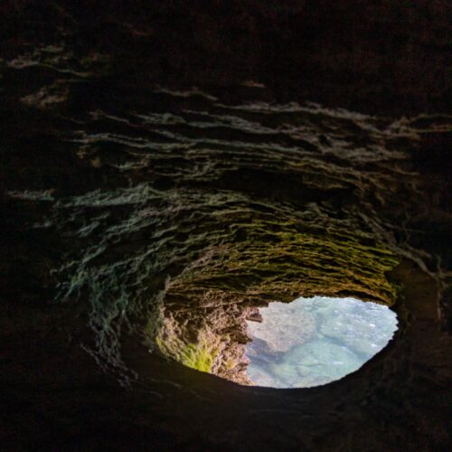 View from inside a dark cave toward a bright opening and water beyond, used as the lead image for a guide to private art foundations and hard-to-access art destinations.