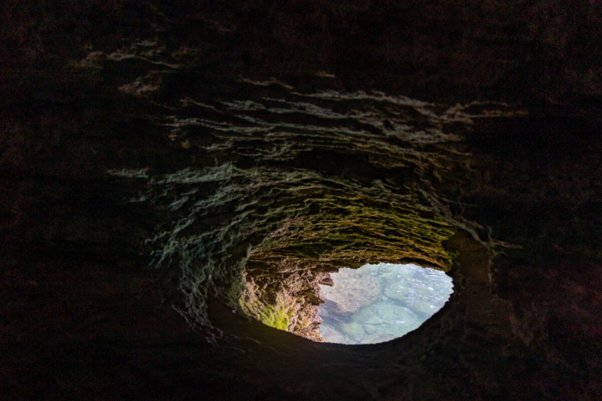 View from inside a dark cave toward a bright opening and water beyond, used as the lead image for a guide to private art foundations and hard-to-access art destinations.