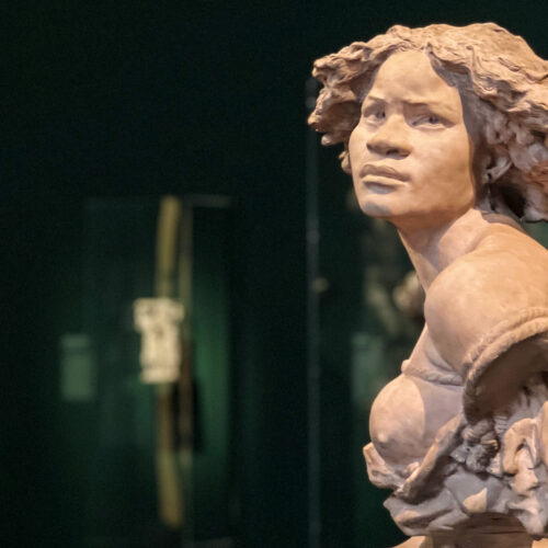 Bronze-toned sculpture of a Black female figure in a museum gallery, photographed in dramatic low light for Dandelion Chandelier’s Juneteenth reading list.