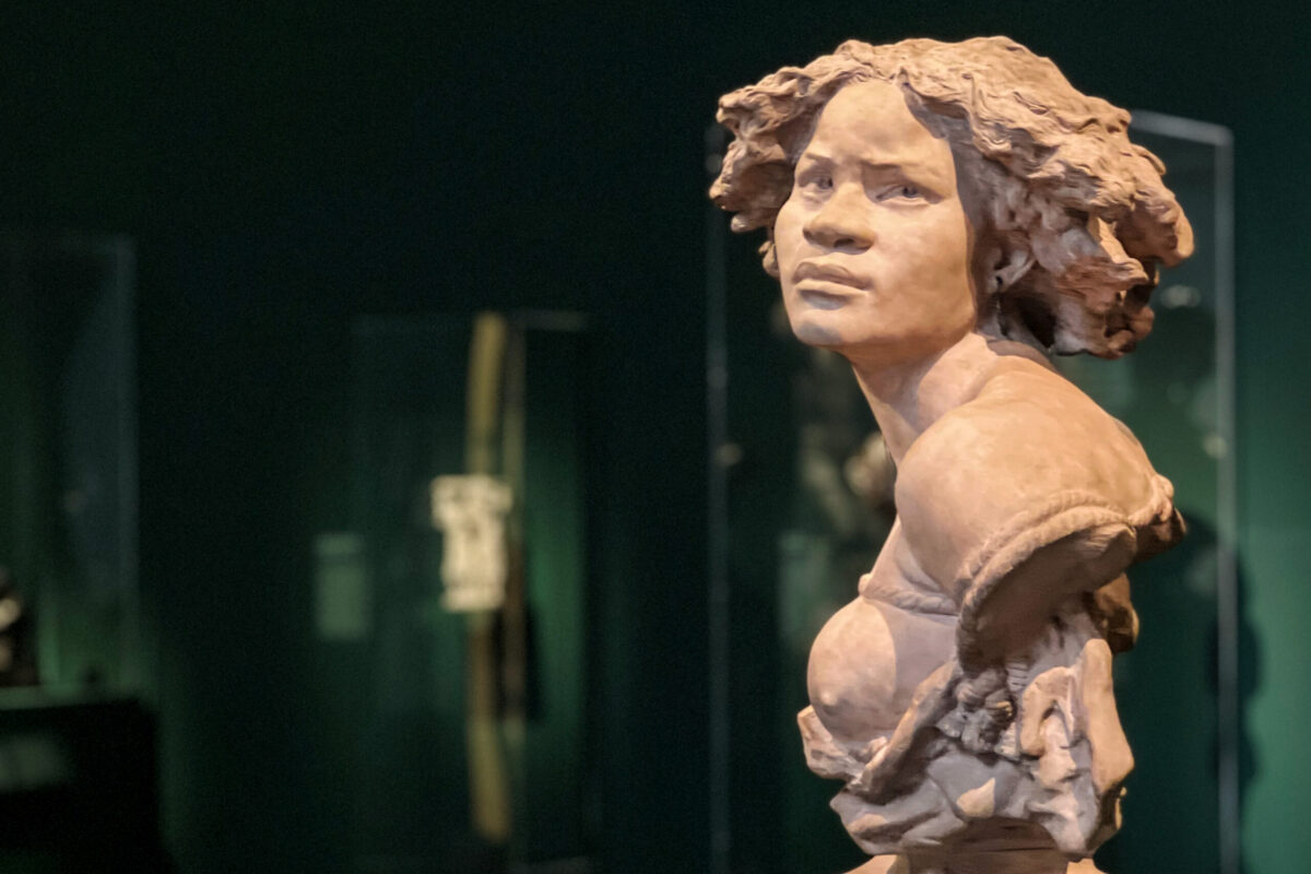 Bronze-toned sculpture of a Black female figure in a museum gallery, photographed in dramatic low light for Dandelion Chandelier’s Juneteenth reading list.