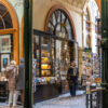 Historic Paris bookstore arcade interior with warm wood arches and bookshop windows, lead image for a post about luxury candles that smell like books and libraries.