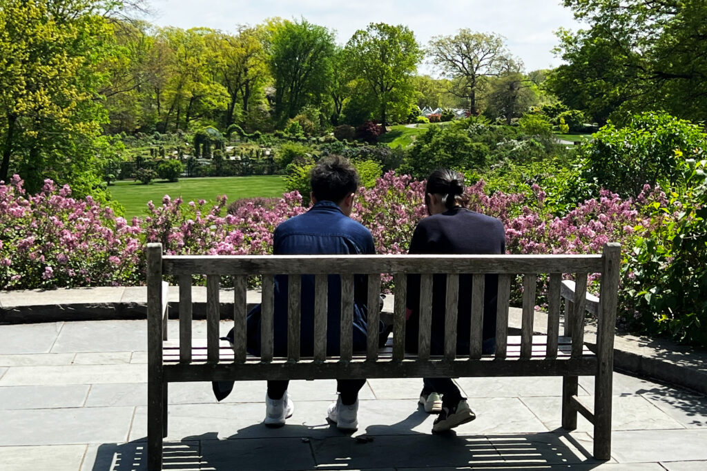 Two visitors seated on a bench overlooking lilacs in bloom at the New York Botanical Garden in the Bronx.