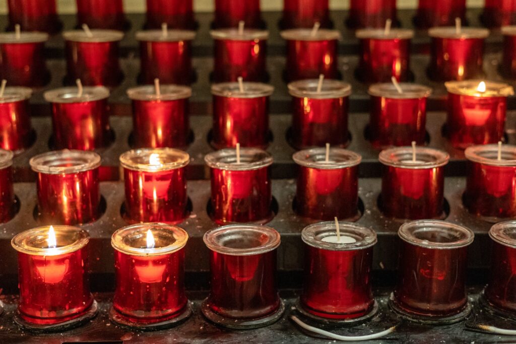 Rows of red votive candles glowing inside a church, with several small flames lit.