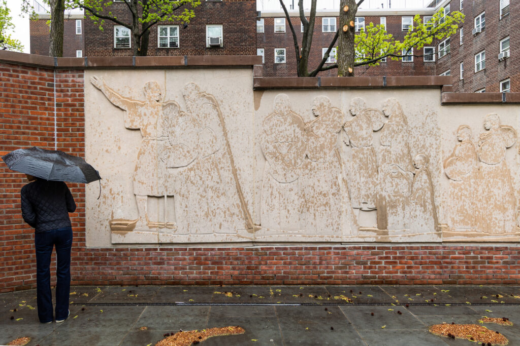 Visitor with black umbrella standing before Richmond Barthé’s Exodus and Dance frieze at Kingsborough Houses in Brooklyn.