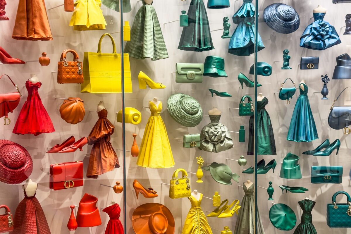 Dior fashion window display arranged by color, from red and orange to yellow, green and teal, illustrating how to wear color well.