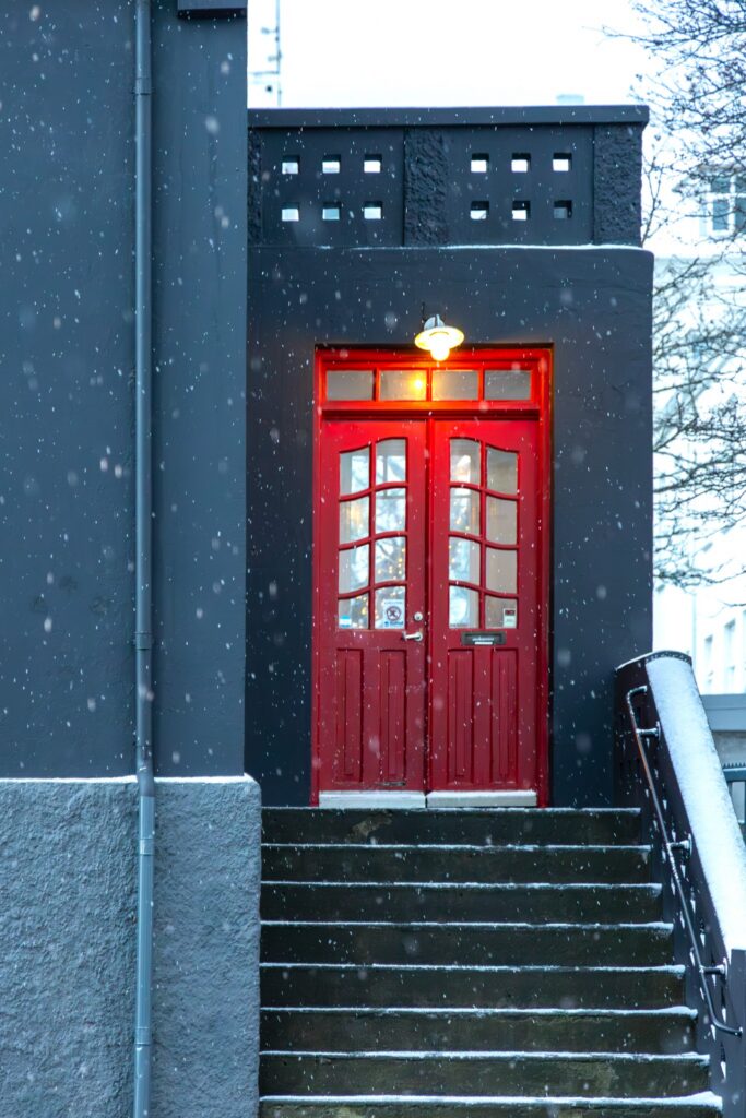 Bright red door against a gray and black building in falling snow, illustrating color as signal, contrast and memorability.