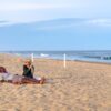Couple sitting on a summer beach near blue water in late light for Dandelion Chandelier’s July reading list.