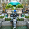 Spring garden fountain at Rockefeller Center with yellow tulips, blue flowers, ferns, and sculptural water figures in New York City.