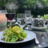 Easy outdoor dinner party table with salad, wine, candlelight, and garden setting for summer entertaining