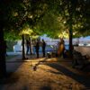 Outdoor jazz band performing under trees at twilight with bridge lights in the background.