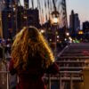 Woman on a New York City bridge at dusk, looking toward city lights, for a guide to where to take visiting foodies in NYC.