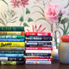 Stacks of the best books of 2026 so far on a table with floral wallpaper for Dandelion Chandelier’s DC120 midyear edit.