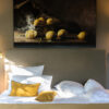 White summer bed with golden accent pillows, warm light and lemon artwork above the headboard.
