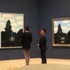 Visitors viewing René Magritte’s The Dominion of Light paintings in a dark blue gallery at SFMOMA.
