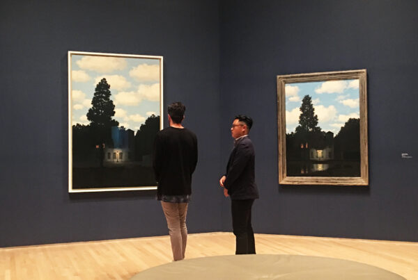 Visitors viewing René Magritte’s The Dominion of Light paintings in a dark blue gallery at SFMOMA.