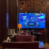 A FIFA World Cup watch party in a wood-paneled private room with leather chairs, wine glasses, a table lamp and the match on television.