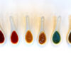 A tasting flight of hot sauces in white ceramic spoons showing red, green, yellow, brown and chili oil sauces.