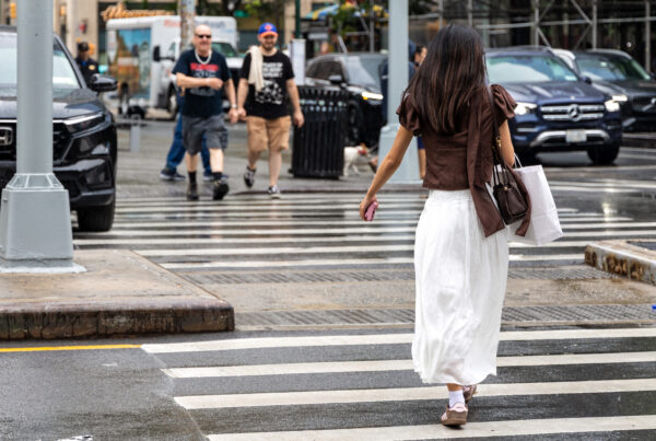 Woman crossing a New York street in a brown top, floating white midi skirt and city sandals during summer rain.