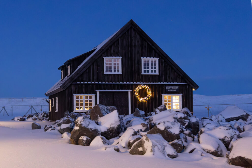 Black Icelandic house glowing warmly against blue twilight snow representing Alabaster Glow.