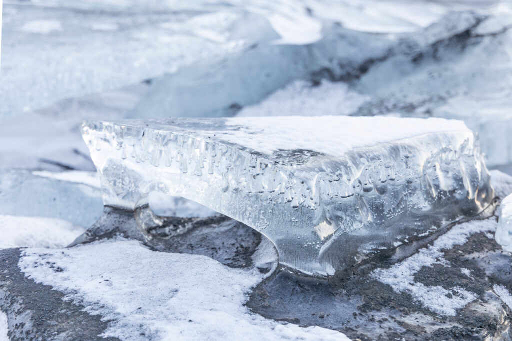 Crystal-clear glacier ice resting on volcanic sand in Iceland representing Ice Blue.