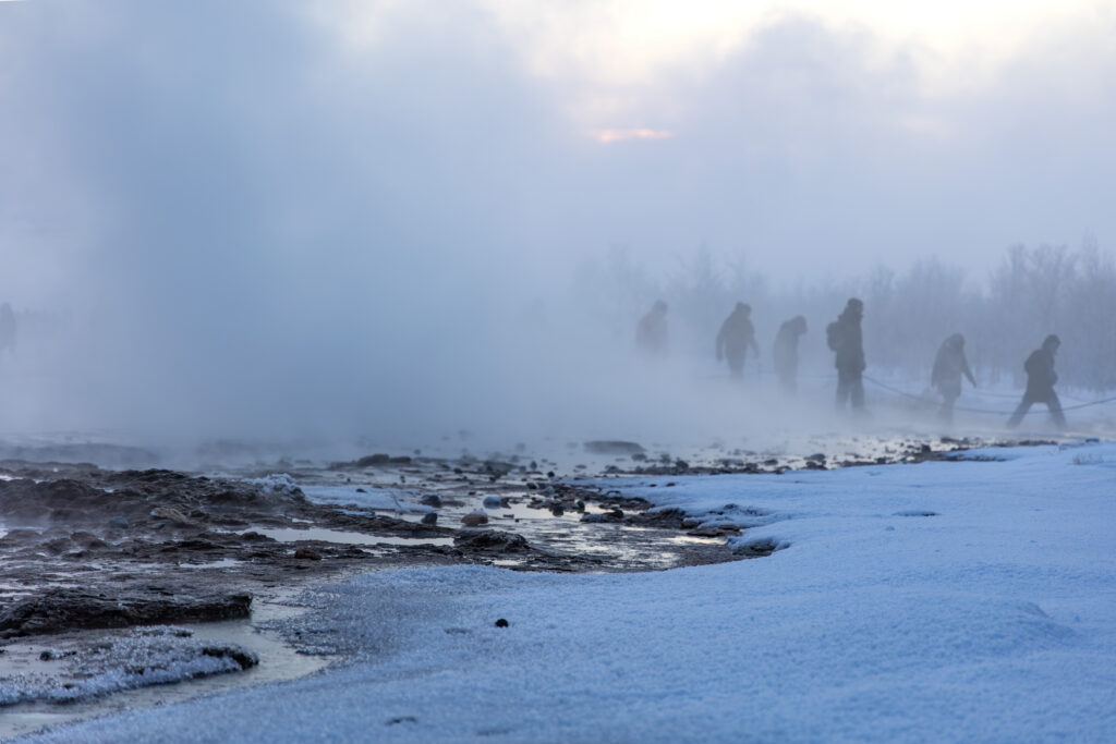 People walking through drifting steam across a snowy Icelandic landscape representing Silver Mist.