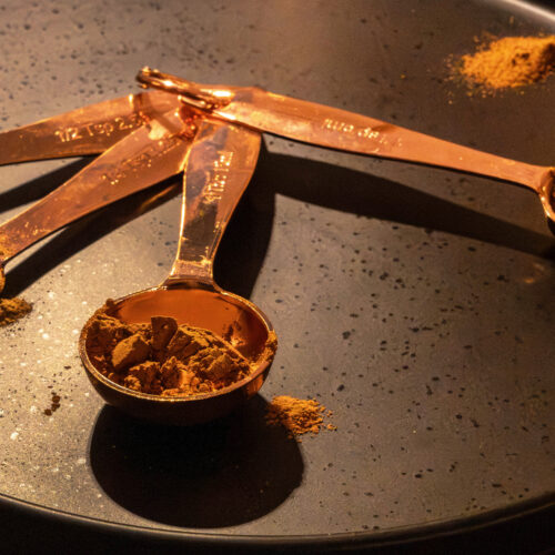 Copper measuring spoons filled with ground spices on a black tray in warm light for Dandelion Chandelier’s best spices to buy online guide.