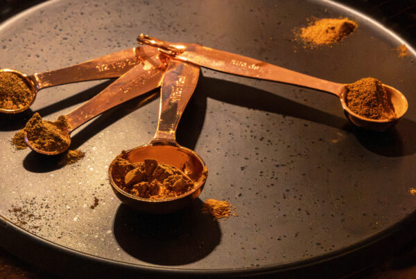 Copper measuring spoons filled with ground spices on a black tray in warm light for Dandelion Chandelier’s best spices to buy online guide.