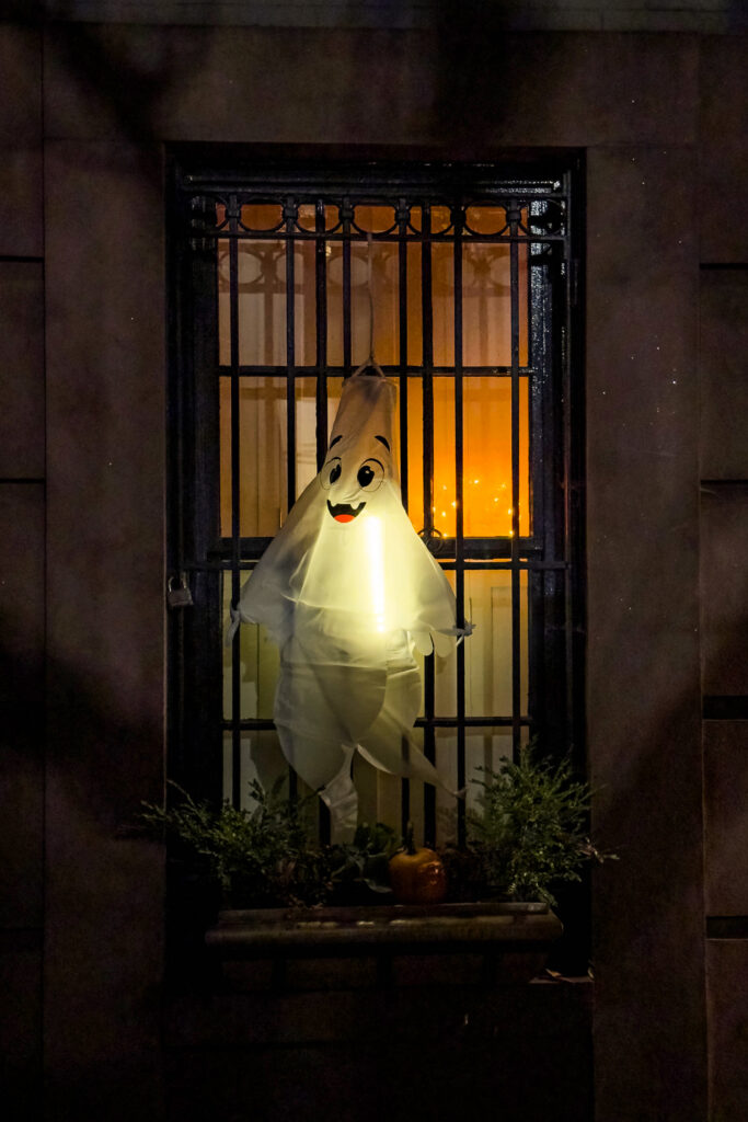Glowing white ghost behind a barred New York window at night during Halloween season, photographed by Pamela Thomas-Graham.