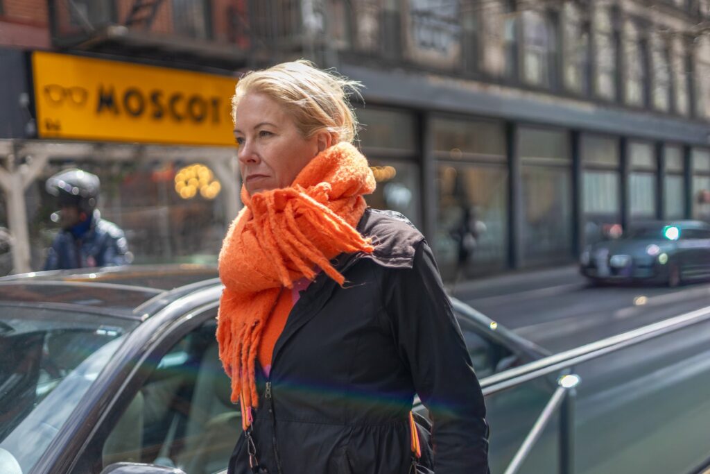 Woman in dark outerwear with an oversized orange scarf on a city street, photographed by Pamela Thomas-Graham.