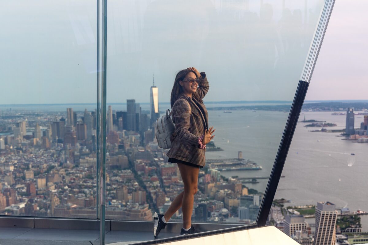 Woman in a checked oversized blazer, sneakers and backpack overlooking New York City, photographed by Pamela Thomas-Graham.