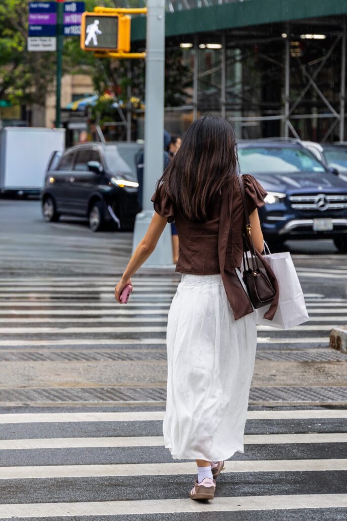 Woman crossing a New York street in a chocolate-brown top, long white skirt and sneakers, photographed by Pamela Thomas-Graham.