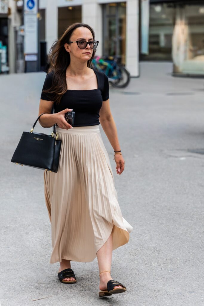 Woman in a black top, long ivory pleated skirt, structured handbag and flat sandals, photographed by Pamela Thomas-Graham.