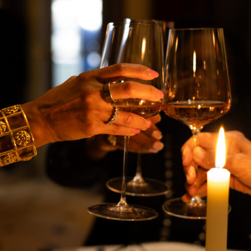 Hands raising wine glasses beside candlelight at an intimate Thanksgiving gathering.