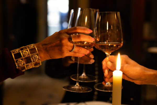 Hands raising wine glasses beside candlelight at an intimate Thanksgiving gathering.