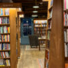 Quiet bookstore aisle lined with science, history and design books under warm pendant lights.
