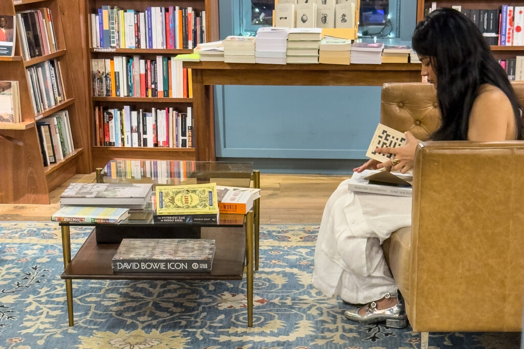 Alt: Woman reading in a leather chair beside art and design books in a New York bookstore.