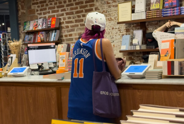 Reader in a Jalen Brunson jersey browsing at the counter of an independent bookstore in New York.