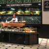 Harrods Vegetable Butchery inside the Food Halls in London, with fresh produce, marble counters and a uniformed staff member.