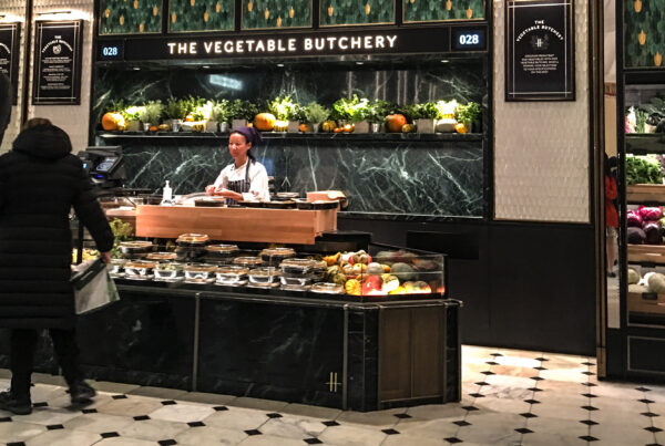 Harrods Vegetable Butchery inside the Food Halls in London, with fresh produce, marble counters and a uniformed staff member.
